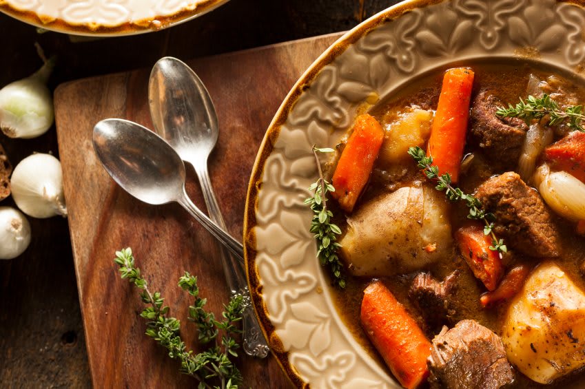 A warm bowl of hearty stew with carrots, potatoes, and fresh herbs served on a rustic wooden table.