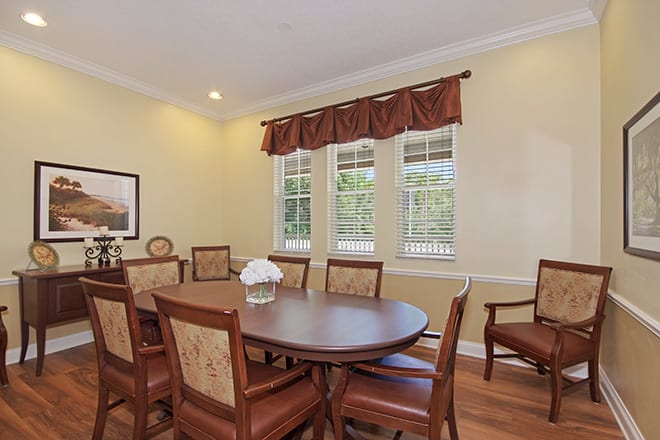 A dining room with a wooden table and chairs, featuring large windows with curtains.