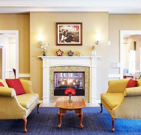 A cozy living room with a central fireplace, surrounded by elegant armchairs and tasteful decor.