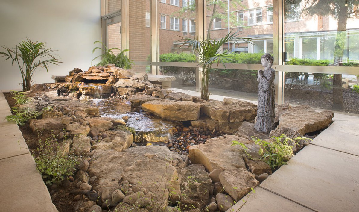 Indoor garden with a stone water feature and statue near large windows letting in natural light.