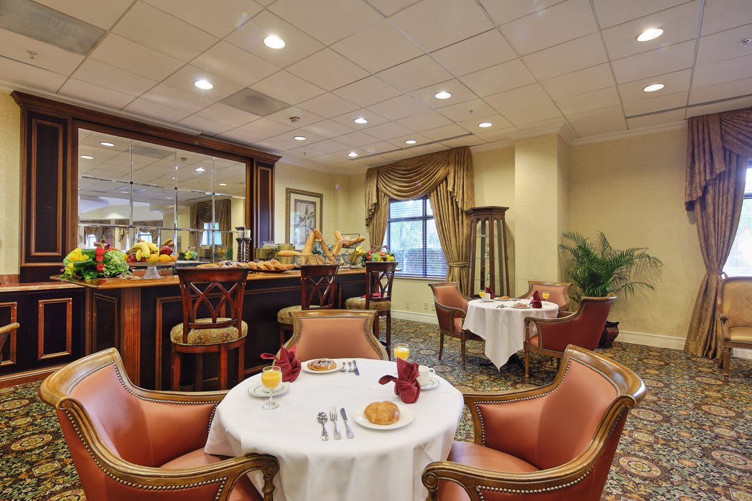 An elegant dining area with tables and chairs, featuring a bar in the background.