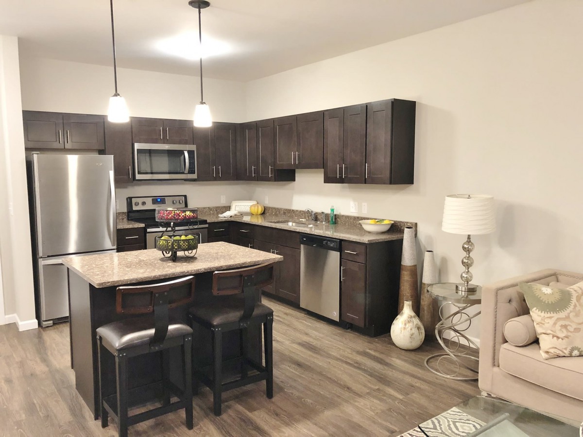 A modern kitchen with dark cabinets, stainless steel appliances, and a central island with pendant lighting.