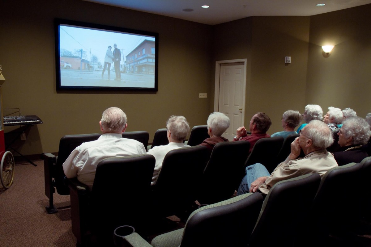 A group of elderly individuals watching a movie in a small cinema room.