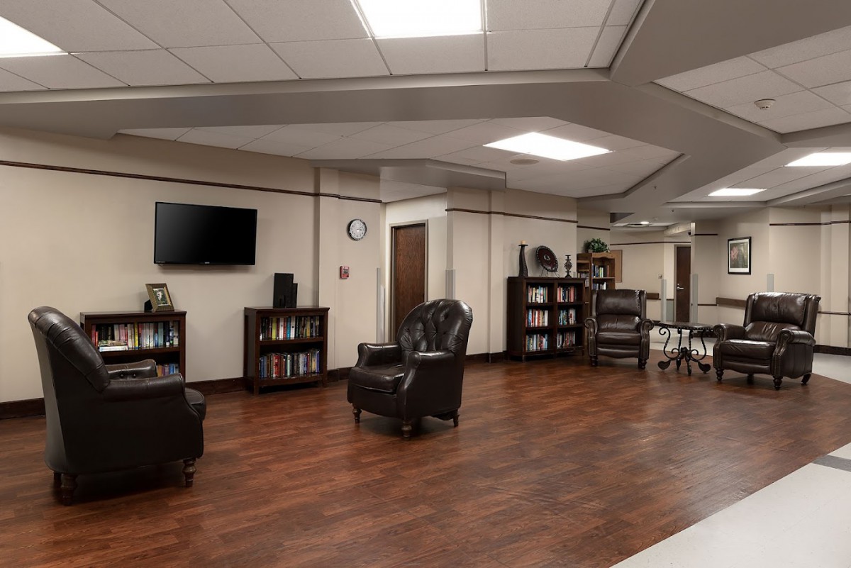 A spacious lounge area featuring leather armchairs, a television, and bookshelves on a polished wood floor.