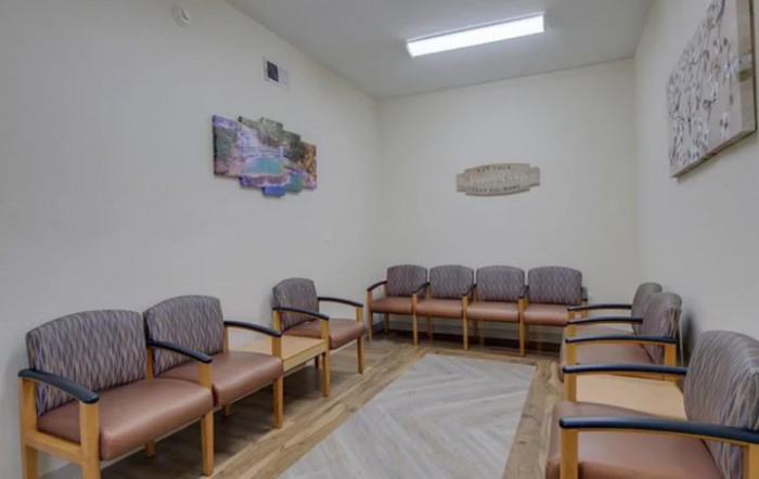 An empty waiting room with several chairs lined up against the walls.