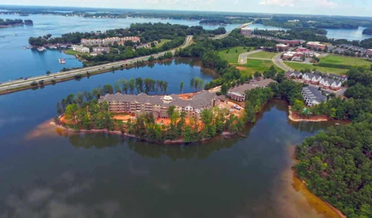Aerial view of a residential building surrounded by a lake and trees.