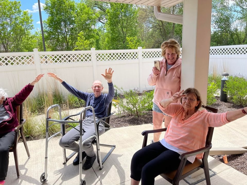 A group of seniors enjoying a sunny day outside, smiling and waving.
