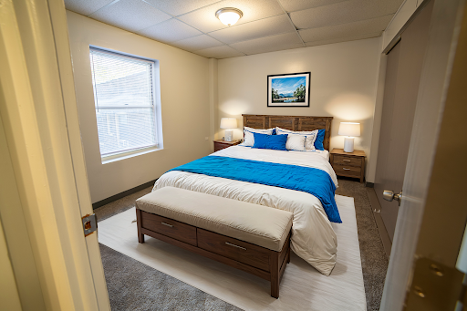 A serene and stylish bedroom featuring a comfortable bed with blue accents, framed artwork, and warm lighting.