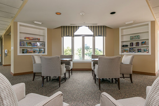 A cozy and well-lit lounge area featuring comfortable chairs, bookshelves, and large windows offering a view.