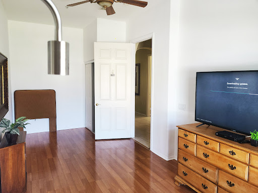 A bright and cozy living room featuring wooden floors, a TV, and a ceiling fan.