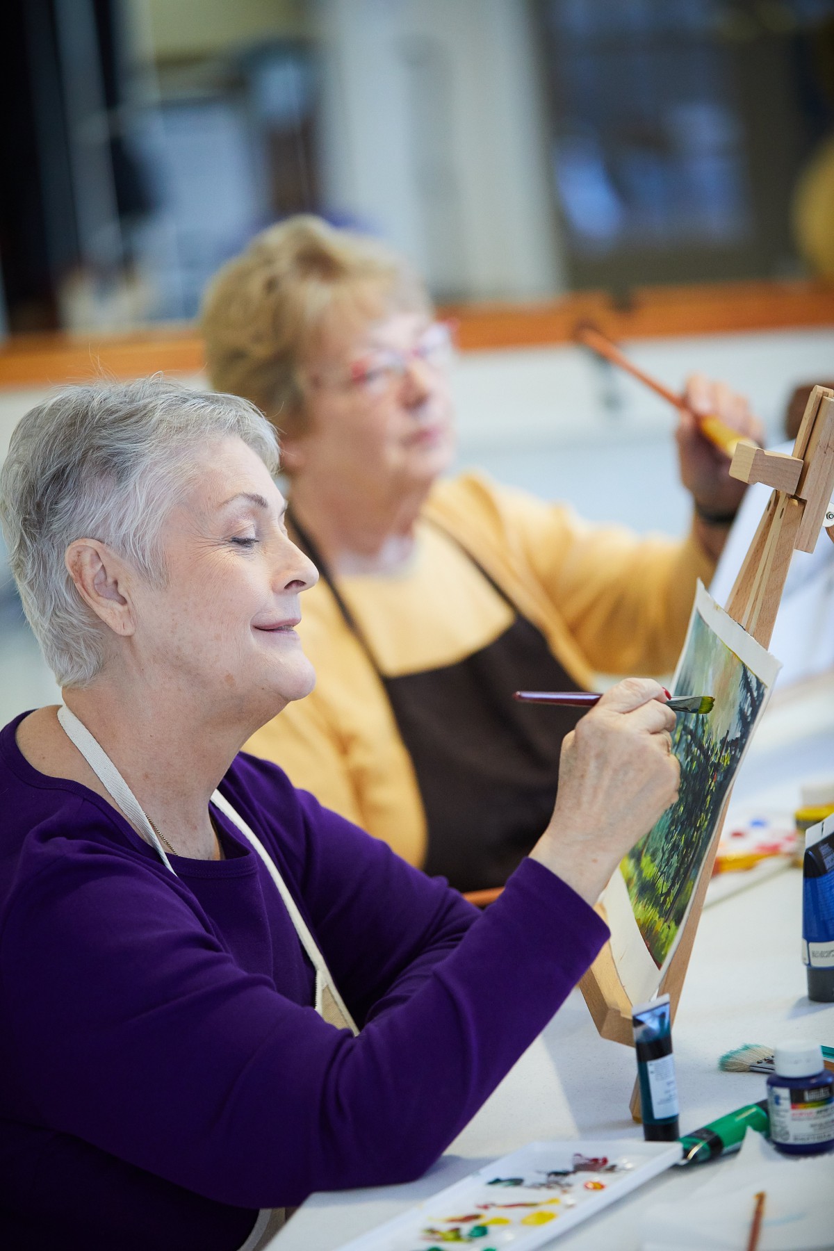 Two senior women focused on painting in an art class.