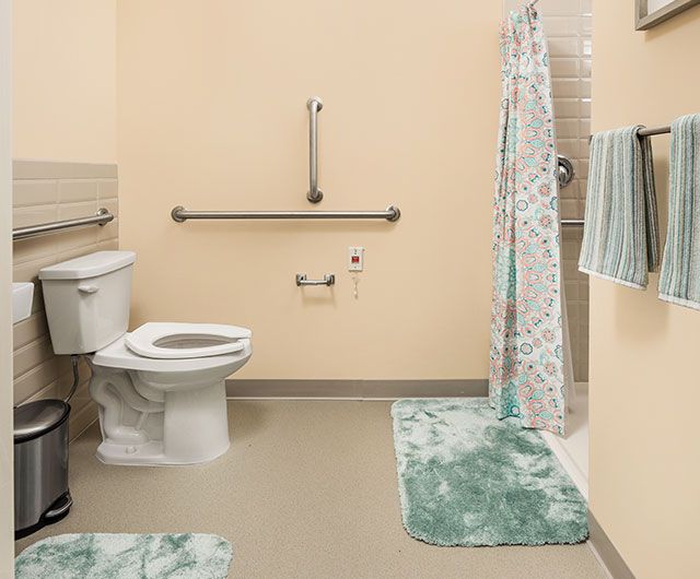 An accessible bathroom with green mats, a shower curtain, and grab bars.