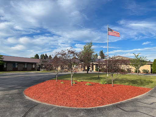 A beautifully landscaped area featuring a building, American flag, and freshly mulched flower beds under a clear blue sky.