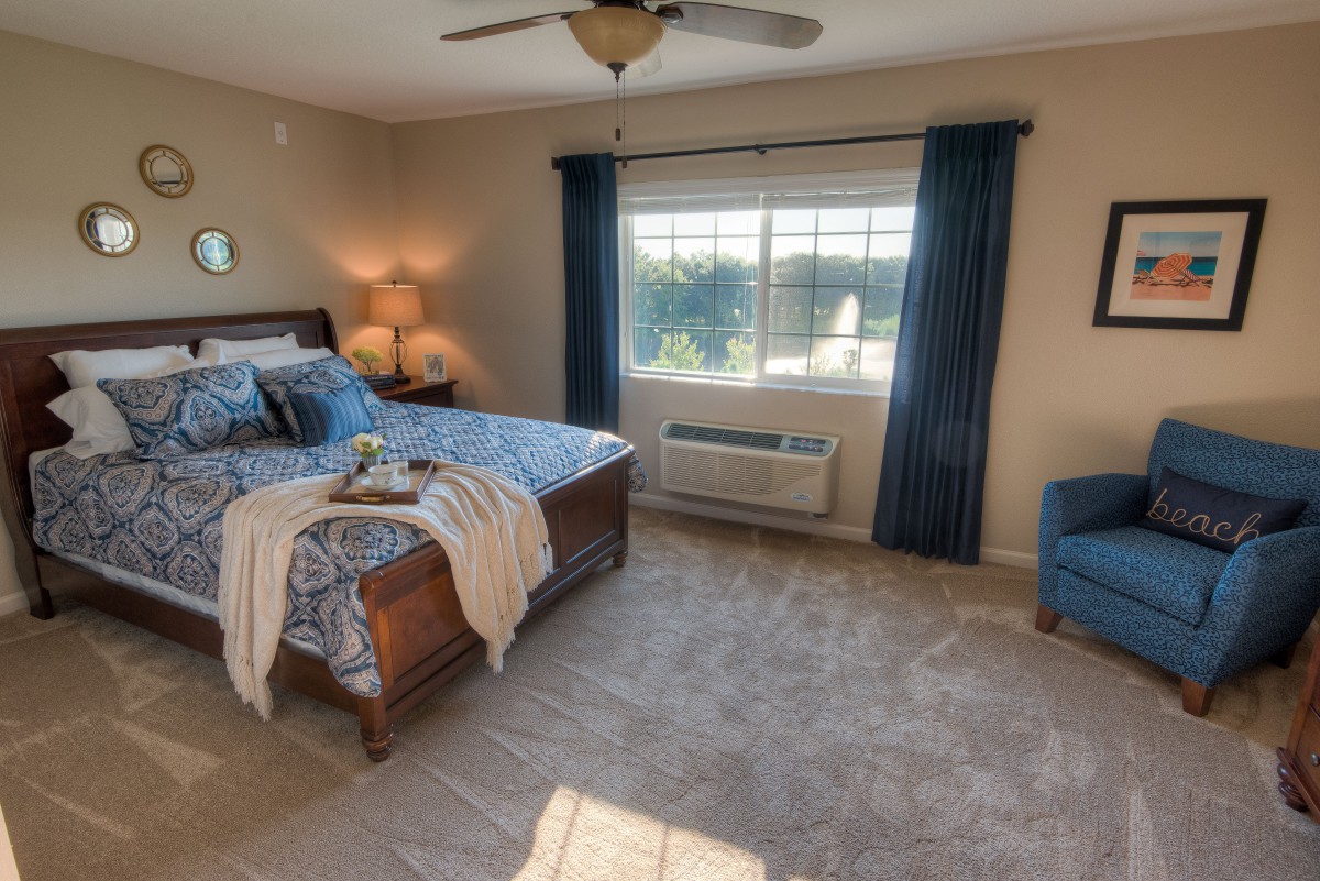 A cozy bedroom with a large bed, blue curtains, and an armchair by the window.