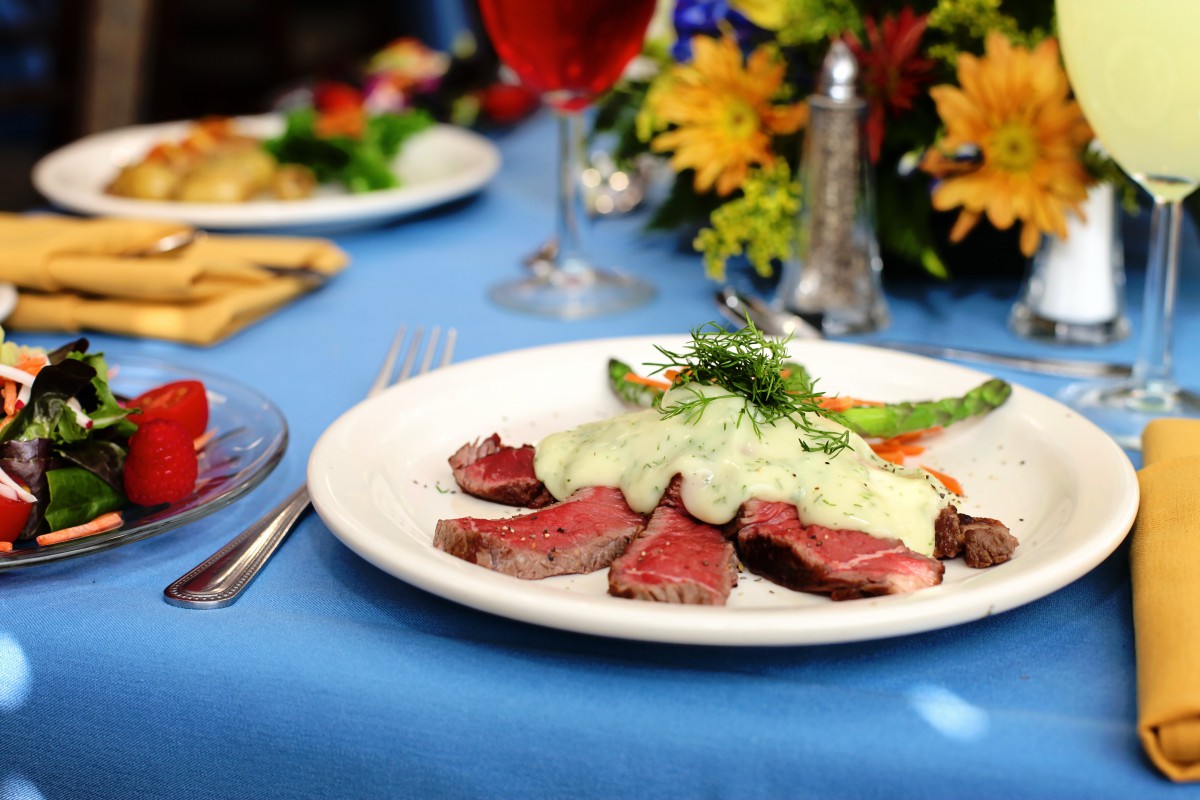 A gourmet steak dinner served with a creamy sauce and vegetables on an elegant table setting.