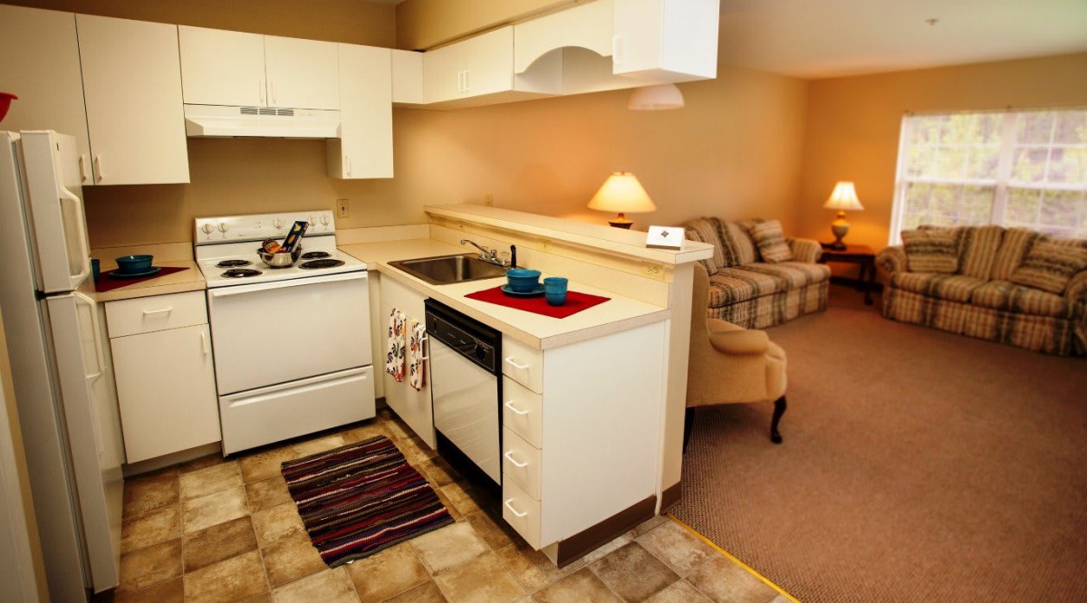A cozy apartment with an open kitchen and living area, featuring white cabinets and modern furnishings.