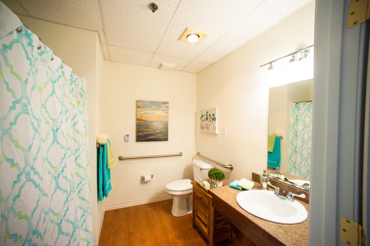 A well-lit bathroom with a sink, mirror, and toilet, featuring teal accents in the towels and shower curtain.