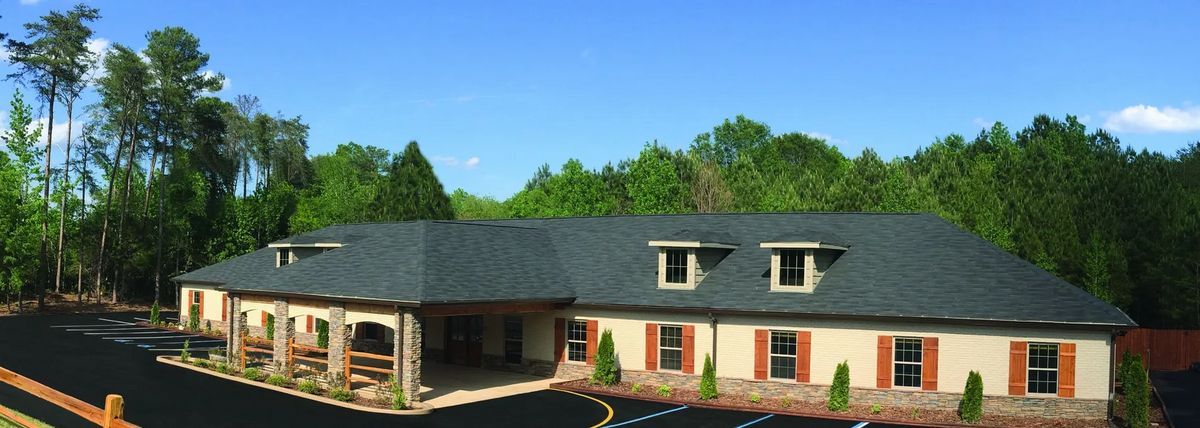 A commercial building with a dark roof and surrounded by greenery under a clear blue sky.