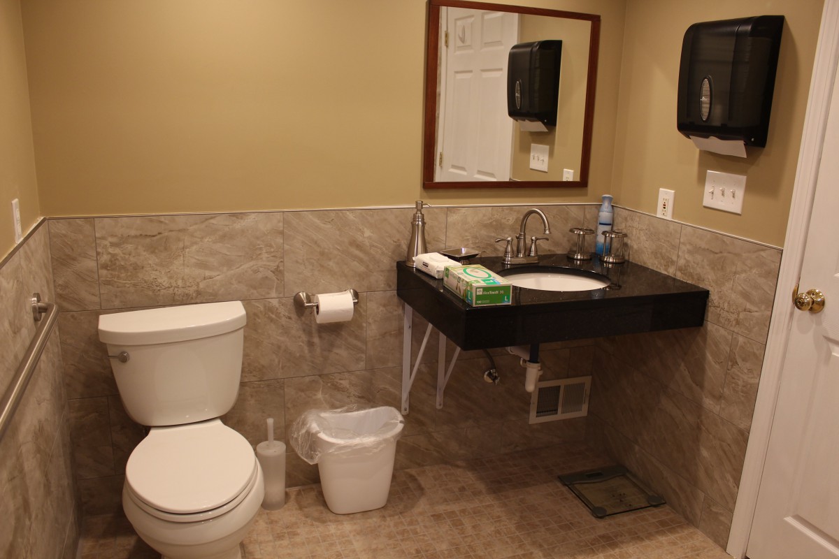 A clean and well-organized bathroom featuring a toilet, sink, mirror, and paper towel dispenser.