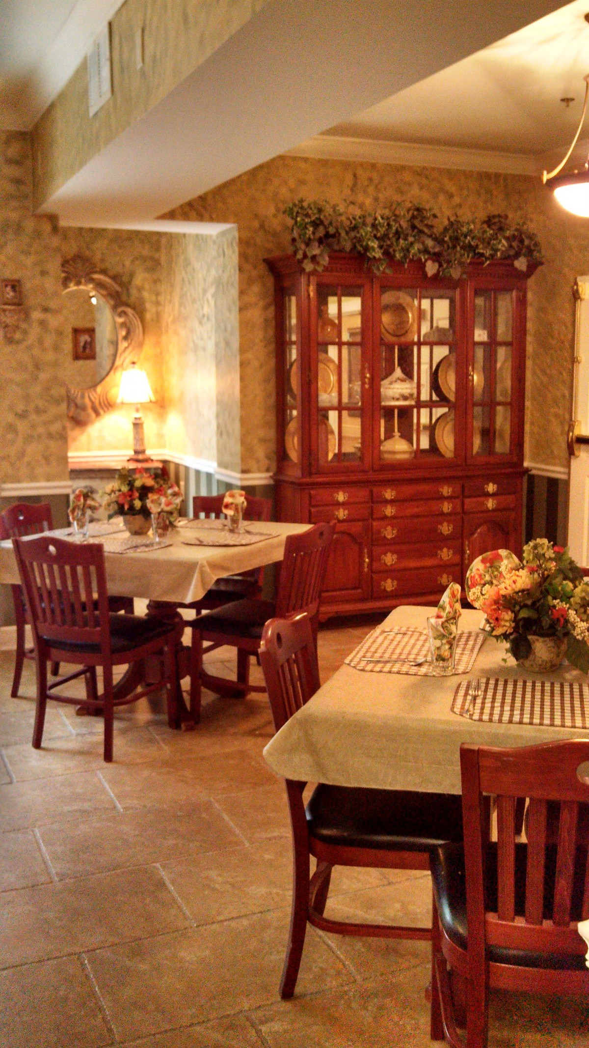 A warmly decorated dining room with a china cabinet and tables set for guests.