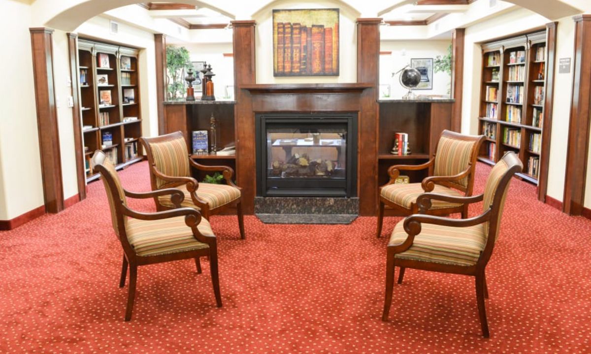 A cozy seating area with four chairs arranged around a fireplace, featuring bookshelves and a painting on the wall.
