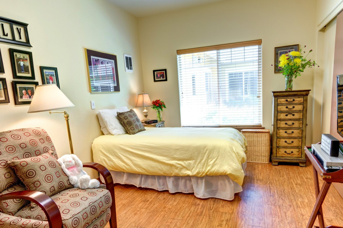 A cozy bedroom with a single bed, armchair, and window letting in natural light.