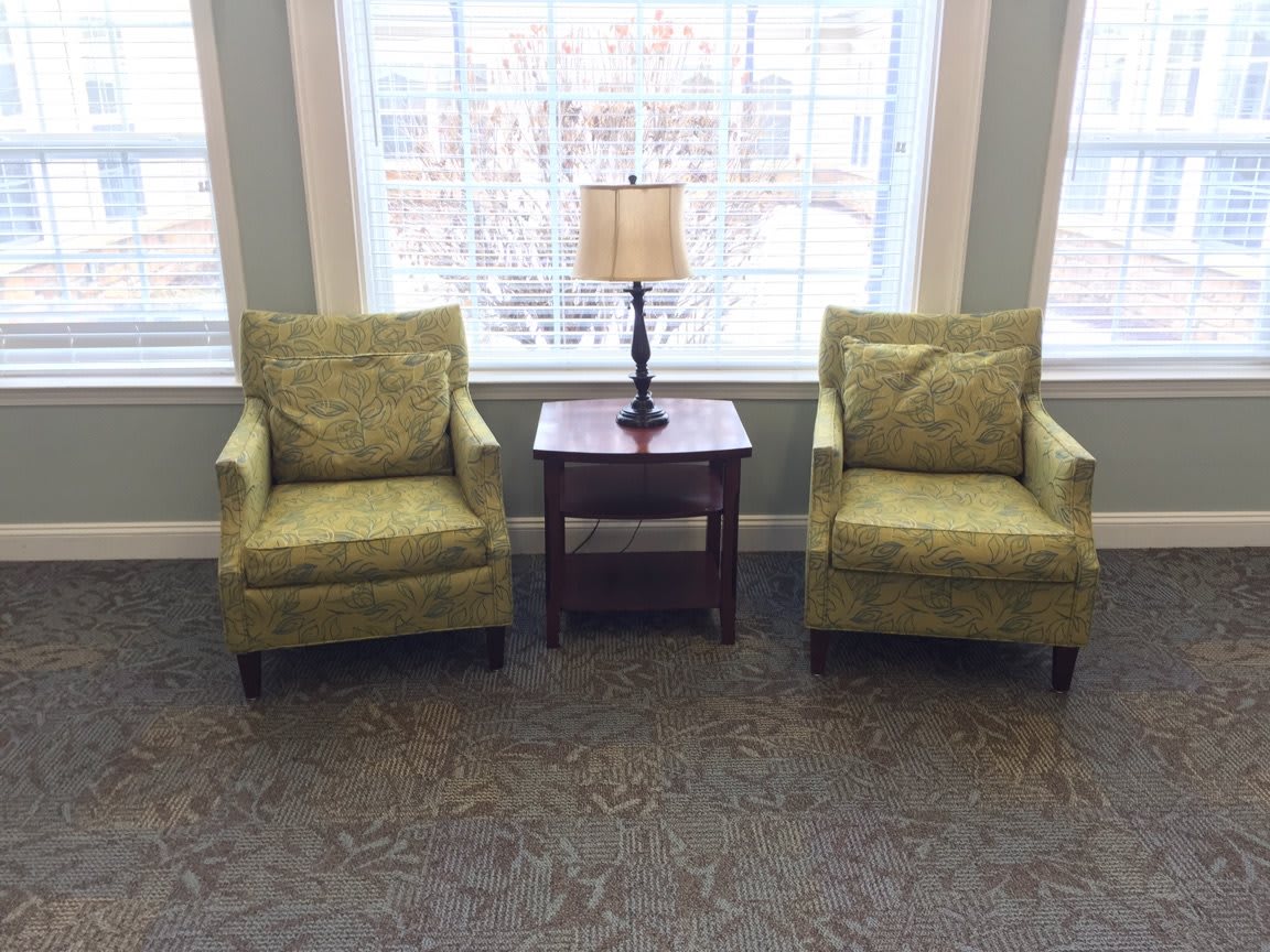 A cozy seating area with two green chairs and a lamp on a side table by the window.