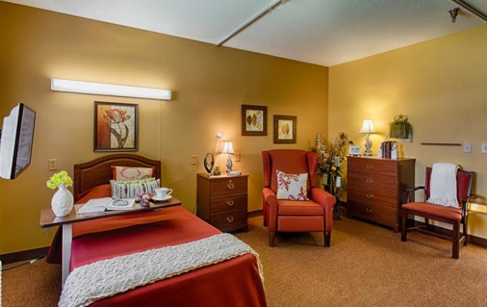 A cozy bedroom with warm lighting, featuring a bed, armchair, and decorative artwork.
