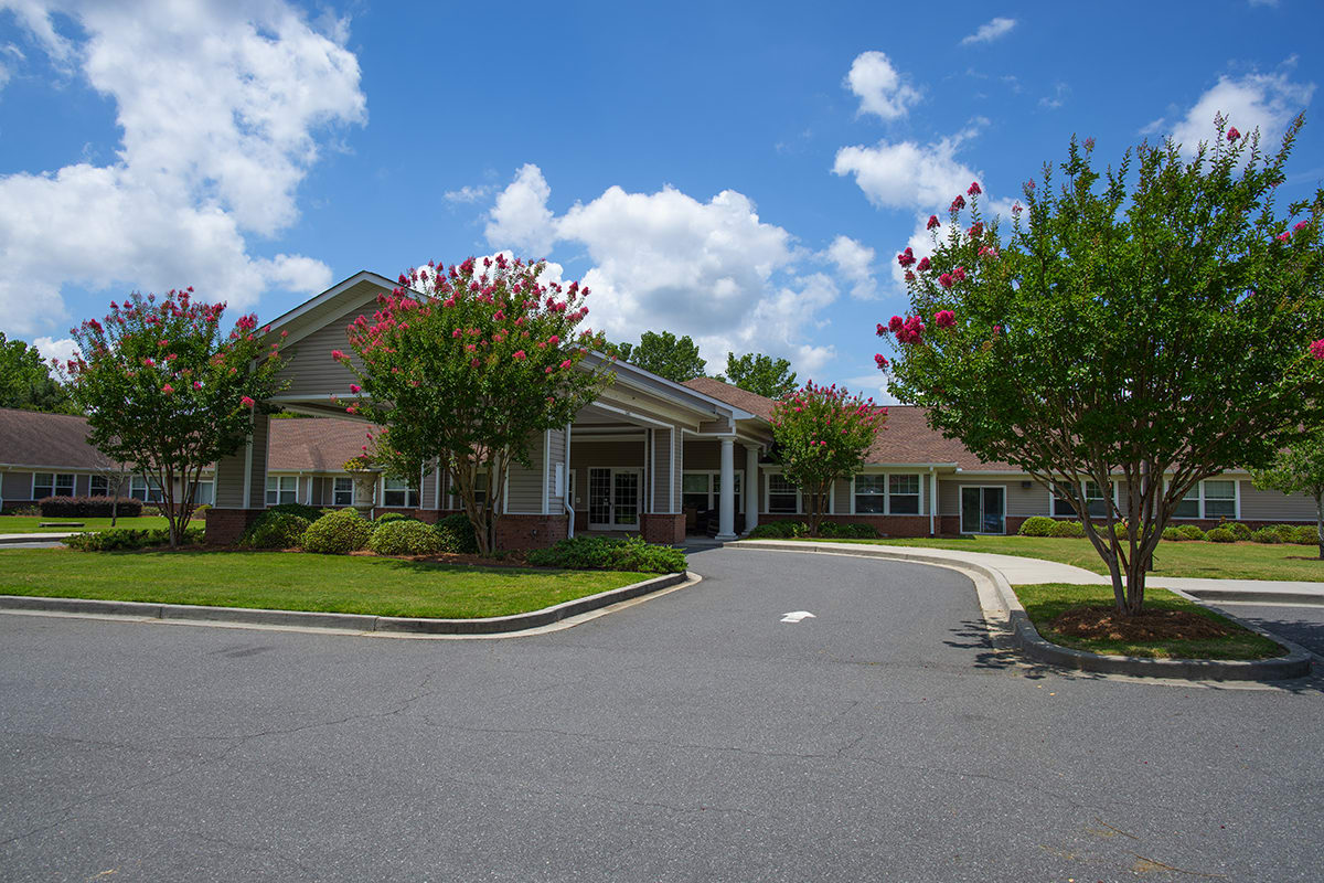 A view of a building entrance surrounded by greenery under a blue sky with clouds.