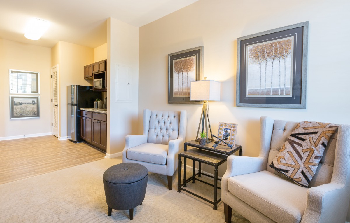 A cozy living room with two armchairs, a small coffee table, wall art, and a view of the kitchenette.