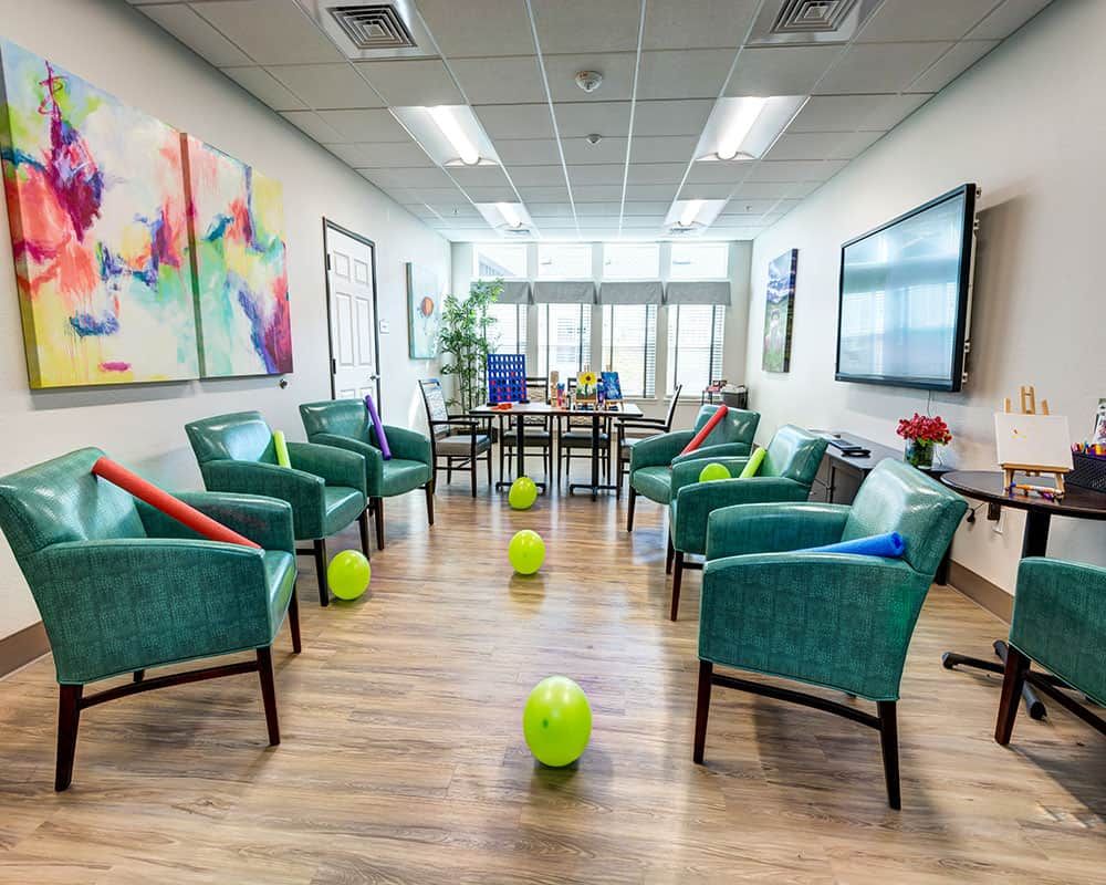 A bright and colorful office meeting room with chairs arranged in a circle, decorated with balloons and artwork on the walls.