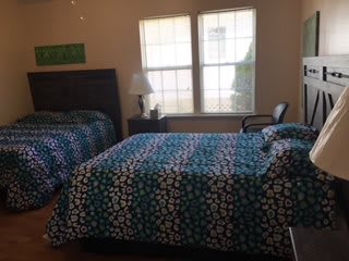 A cozy bedroom featuring two beds with patterned bedding, a lamp, and a window allowing natural light.