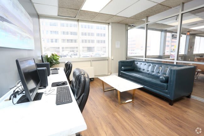 A modern office space with computers on desks, a comfortable sofa, and large windows.
