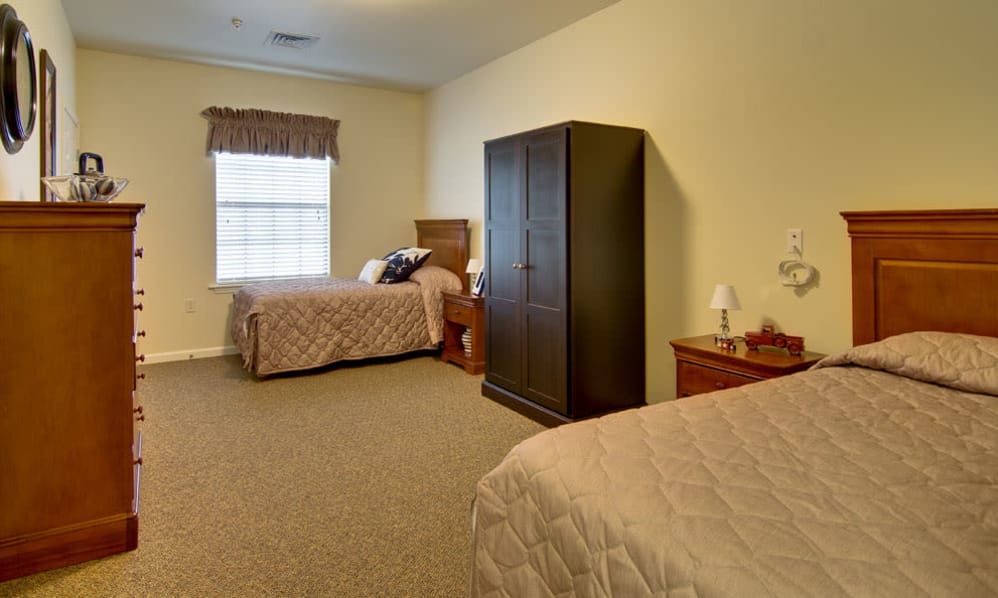 A cozy bedroom featuring two twin beds, a wardrobe, and bedside tables with a window providing natural light.