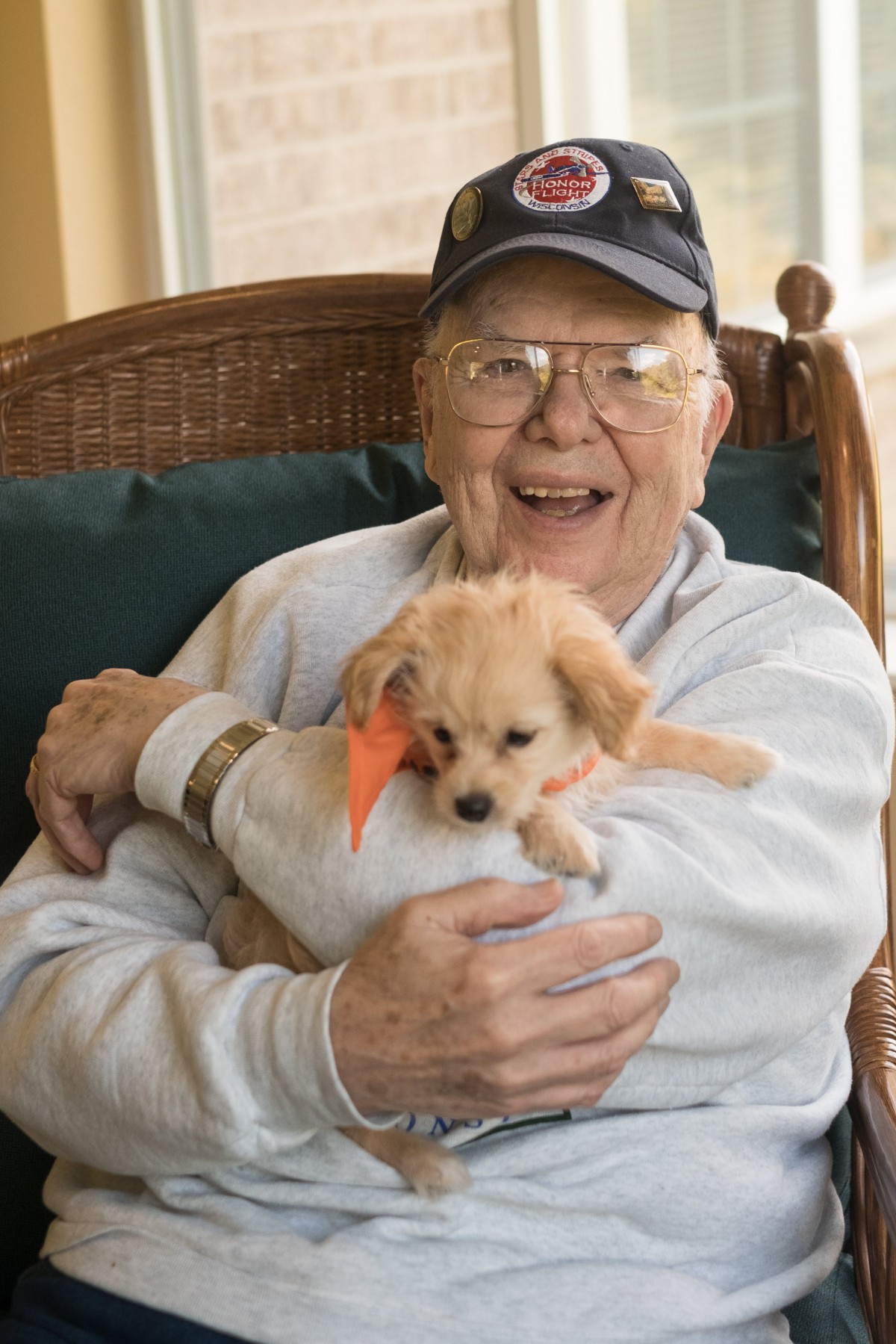 An elderly man happily holding a puppy indoors.
