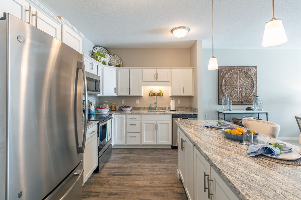 A modern kitchen featuring stainless steel appliances, white cabinets, and an island with a granite countertop.