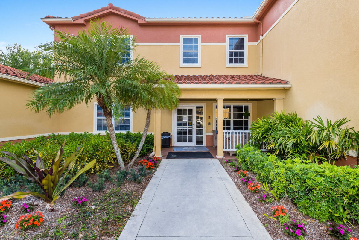 A welcoming house entrance with a neatly landscaped garden and a palm tree.