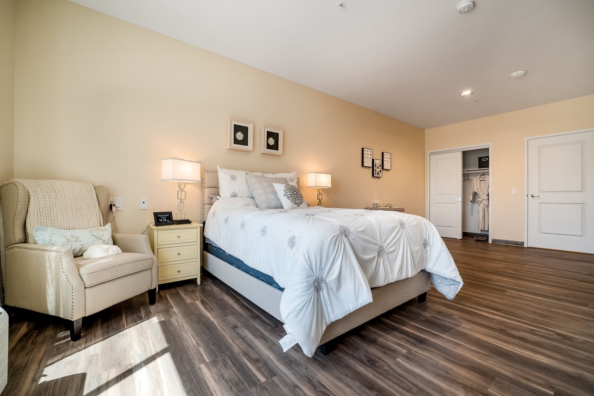 A modern bedroom with wooden flooring, featuring a cozy bed, lamps, and stylish decor.