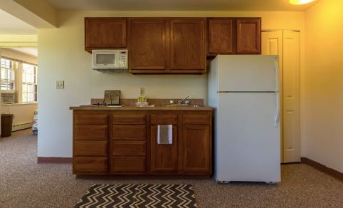 A compact kitchen setup with wooden cabinets, a white refrigerator, and a microwave above the counter.
