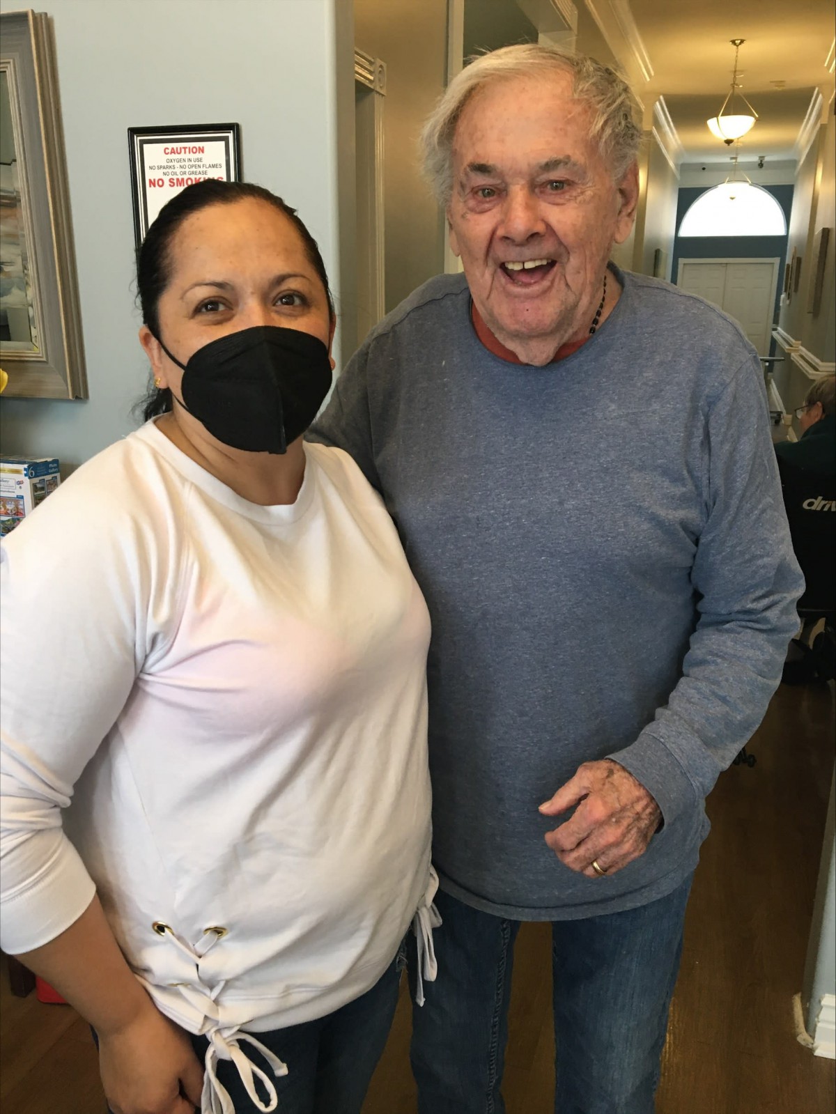 A friendly moment captured indoors with two people smiling, one wearing a mask.