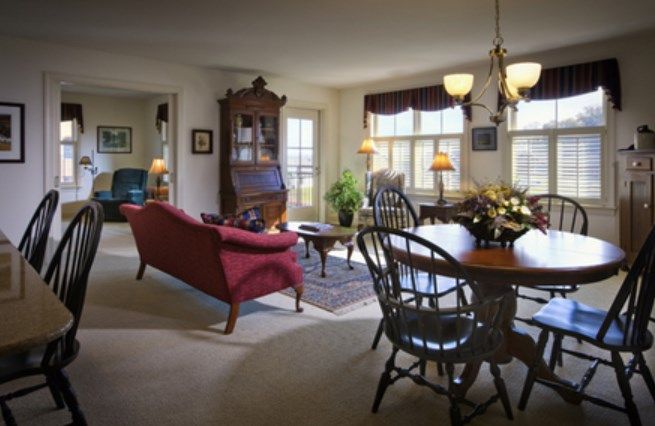 A traditional living room with a red sofa and a dining area featuring wooden furniture, warmly lit by a chandelier.