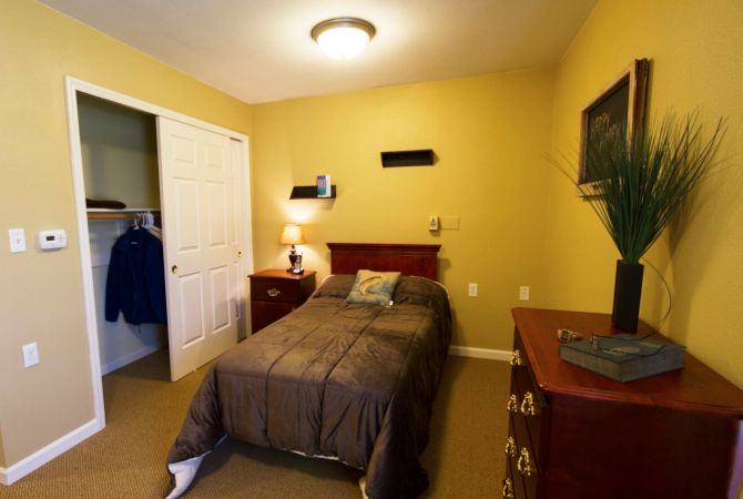 A cozy bedroom with a single bed, nightstand, and dresser in warm yellow tones.