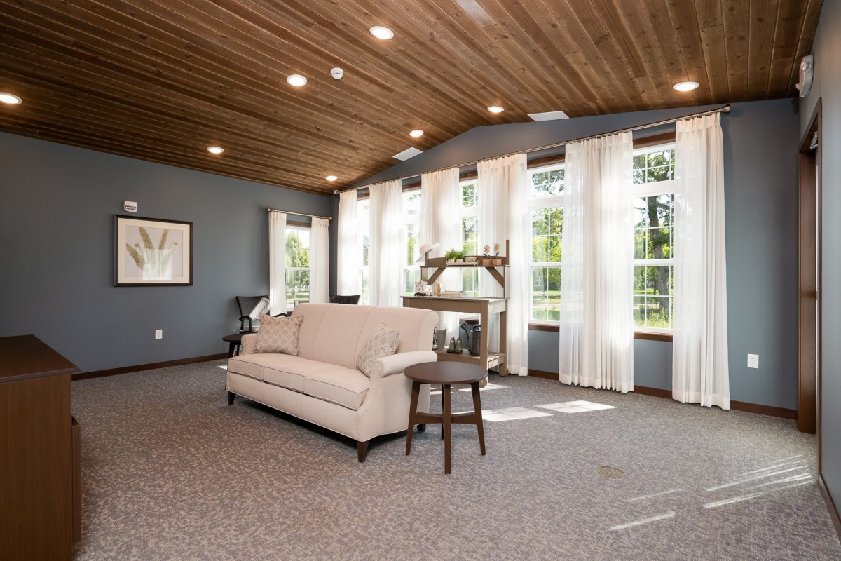 A spacious living room with large windows, a cozy sofa, and a wooden ceiling allowing ample natural light.