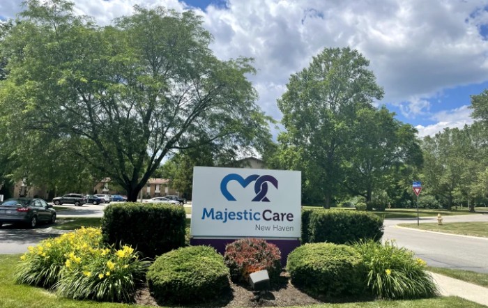 A sign for Majestic Care surrounded by lush greenery and trees.