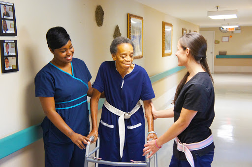 Caregivers assisting an elderly woman with mobility in a healthcare setting.