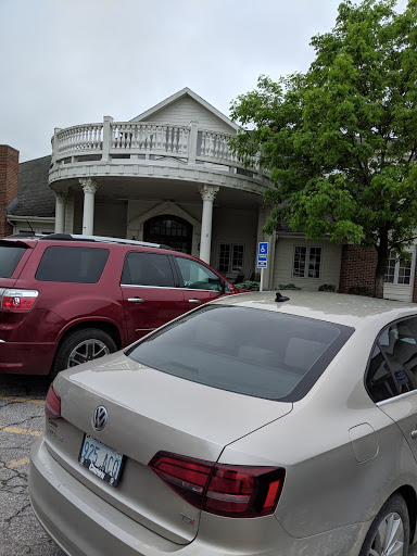 A view of a building with a balcony, surrounded by parked cars and trees under a cloudy sky.