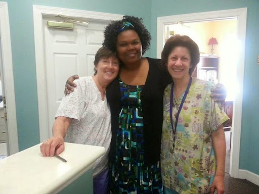 A group of three women smiling together in a healthcare setting.