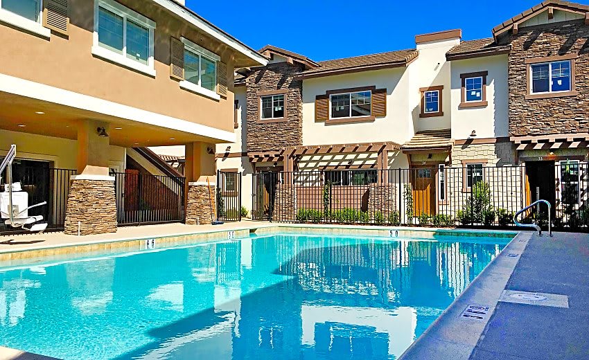 A modern residential building with a clear blue swimming pool in front.