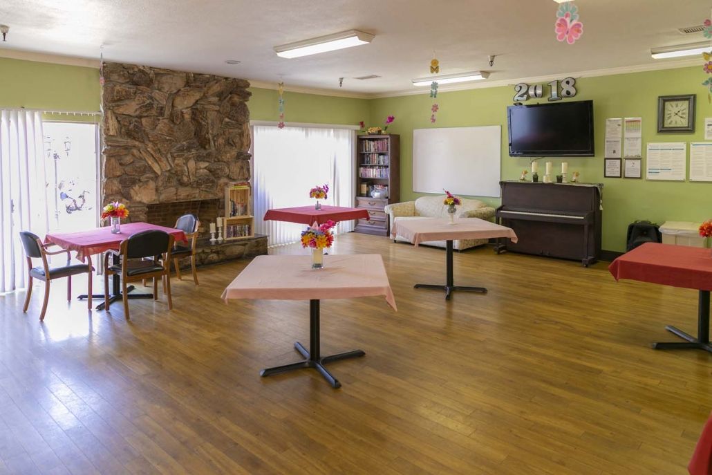 A spacious room with wooden floors featuring tables, chairs, a television, and a piano.