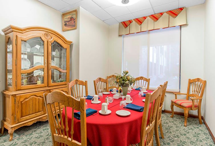 A cozy dining room with a round table set for tea, featuring a red tablecloth and wooden chairs.